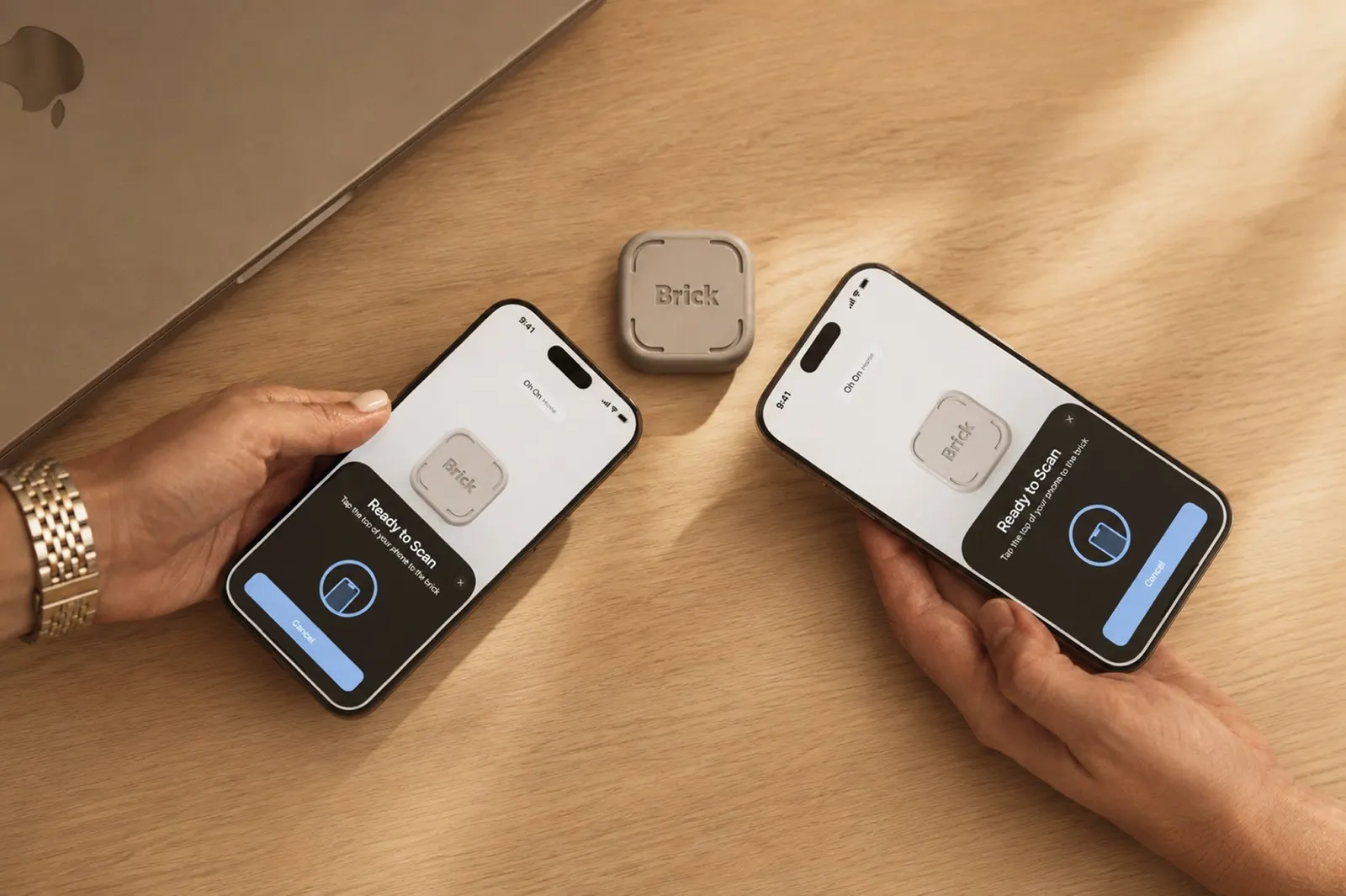 two hands holding iphones on either side of a small brick nfc tag sitting on a wooden desk