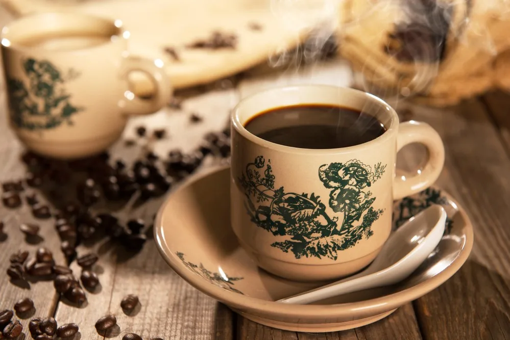 a cup of malaysian kopi coffee steaming on a wooden table, coffee beans scattered around