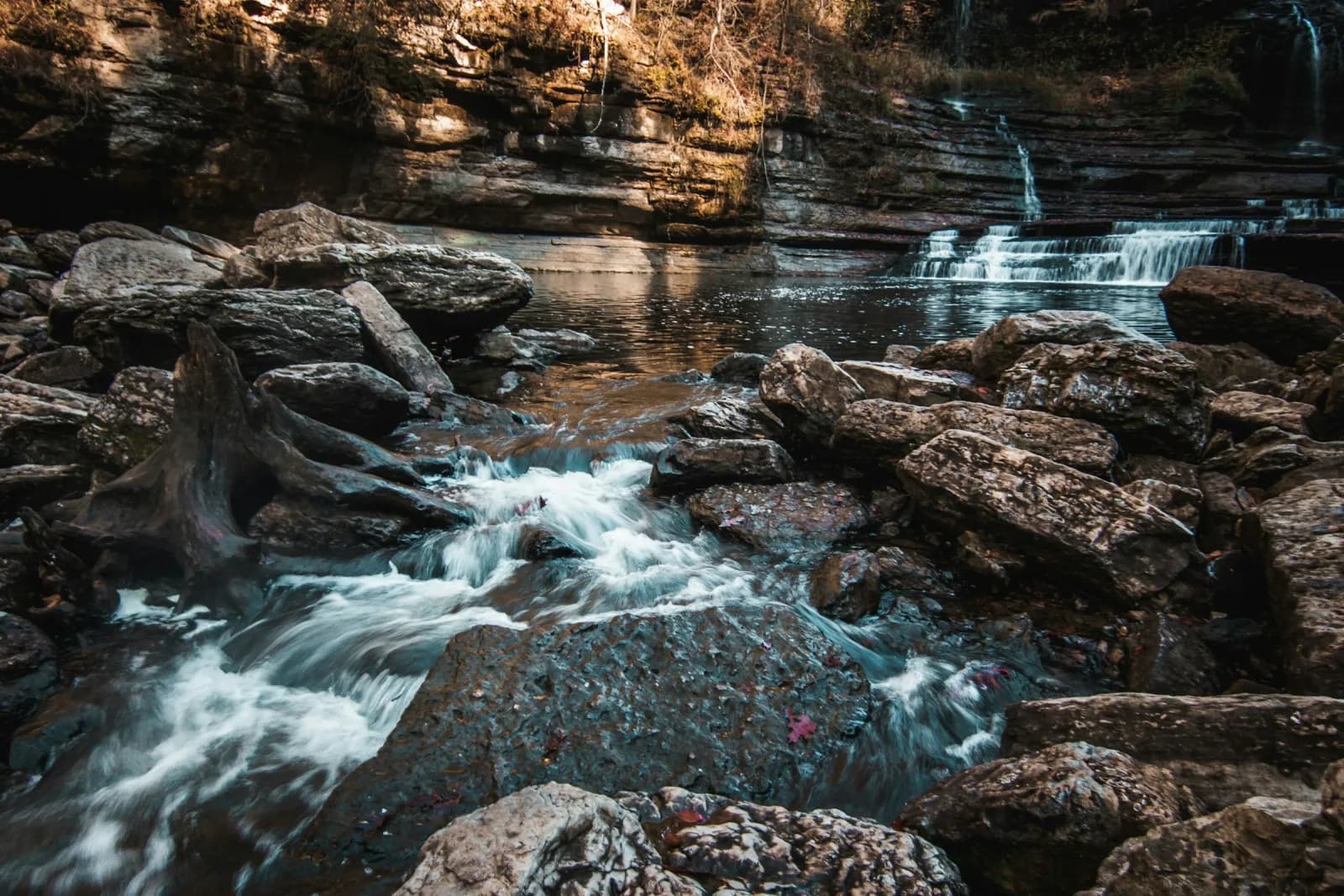 a long exposure photo of a mountain stream, the water blurred into smooth white lines as it runs around dark rocks